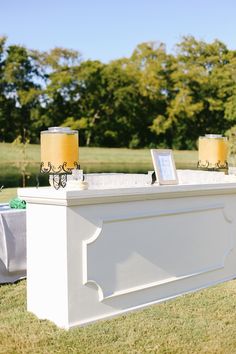 a white table with two yellow lamps on it and some tables cloths in the background