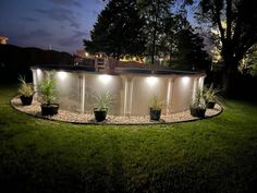 a fenced in area with plants and lights on it at night, surrounded by grass