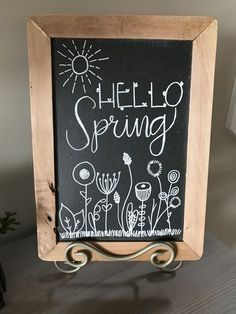 a chalkboard sign with the words hello spring written on it and flowers in front