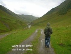 a man walking down a dirt road in the mountains with a backpack on his back