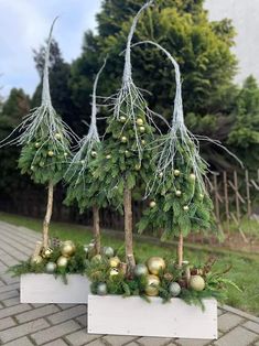 three white planters filled with green and gold ornaments sitting on top of a brick walkway