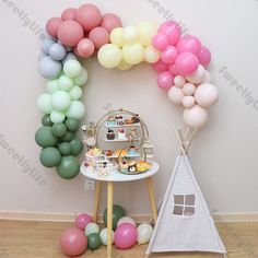 an arch made out of balloons and cake on a table with a teepee tent next to it