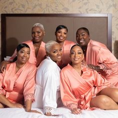 a group of women sitting on top of a bed in matching pink robes and white pants