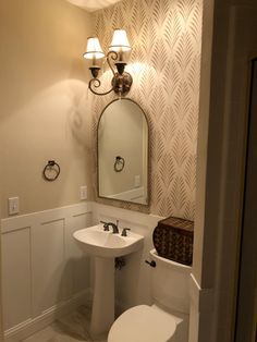 a white toilet sitting next to a sink in a bathroom under a mirror and lights