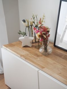 flowers in a vase sitting on top of a wooden counter next to a framed photograph