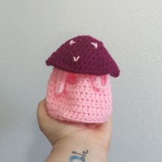 a small crocheted mushroom hat on top of a pink and purple knitted beanie