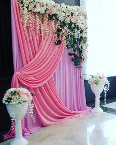 pink and white flowers are hanging on the wall in front of an open window with drapes