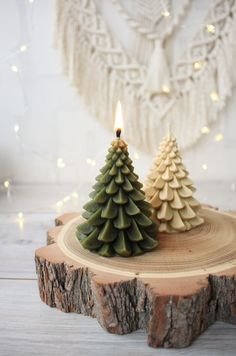 two small christmas trees sitting on top of a piece of wood next to a lit candle