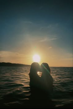 two people kissing in the water at sunset