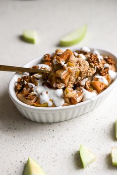 a bowl filled with granola and apple slices on top of a white counter next to sliced apples