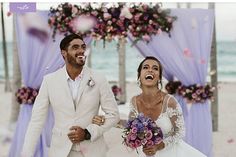 a bride and groom walking down the aisle at their beach wedding in front of an archway decorated with flowers