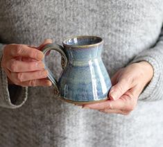 a woman holding a blue and white coffee mug in her right hand while wearing a gray sweater