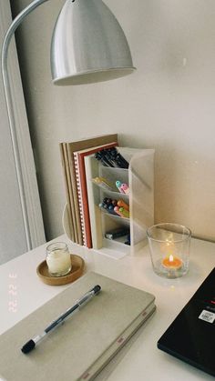 a laptop computer sitting on top of a white desk next to a cup and candle