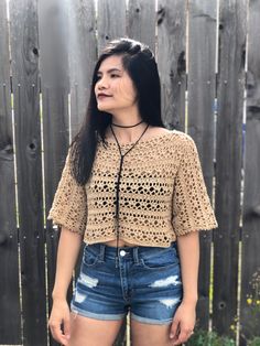 a woman standing in front of a fence wearing shorts and a crochet top