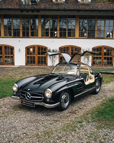 an old black mercedes sports car parked in front of a large white building with lots of windows