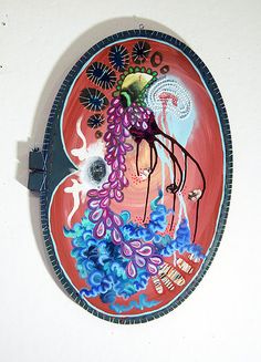 a red plate with blue and purple designs on it is hanging from the wall in front of a white wall