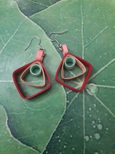 two pairs of red and pink earrings sitting on top of a green leaf covered ground