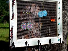 an old window is decorated with colorful buttons and chains hanging on the tree trunk in front of a grassy area