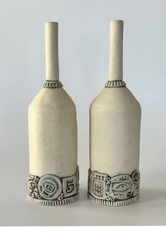 two white vases sitting side by side with designs on the top one and bottom