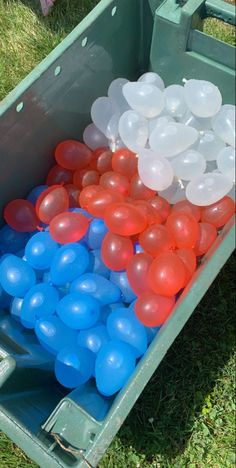 red, white and blue balloons are in a green container on the grass with other balloons