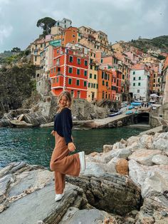 a woman is standing on rocks near the water in front of some buildings and boats