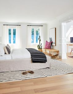 a white bed sitting on top of a hard wood floor next to two large windows