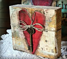 a red heart shaped box with a key attached to it sitting on top of a table