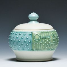 a white and green bowl with a lid on it's side, sitting against a gray background