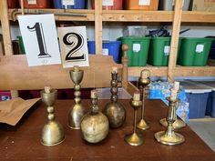 brass candlesticks and numbers are sitting on a table in front of shelves with bins