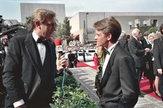 two men in tuxedos talking to each other on the red carpet at an event