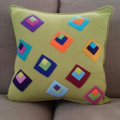 a green pillow with colorful squares and a crown on it's head sitting on a couch