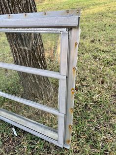 an old window sitting in the grass next to a tree with rusted metal rivets