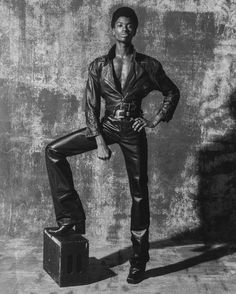 a man standing on top of a piece of luggage in front of a concrete wall