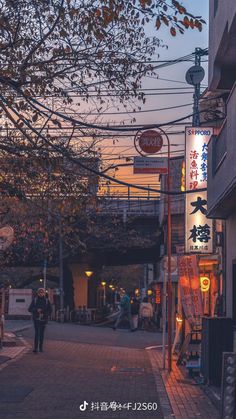 a person walking down the street in front of some buildings at dusk with lights on