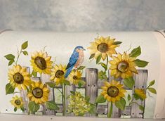 a mailbox decorated with sunflowers and a blue bird sitting on the fence