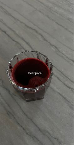 a glass filled with red liquid sitting on top of a marble table next to a bottle of wine