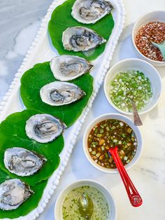 a platter filled with oysters on top of a green leaf covered table next to bowls of condiments