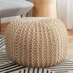 a round knitted poufle sits on a rug in front of a chair