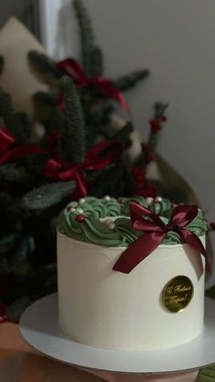 a white cake with green frosting and red ribbon on top sitting on a plate