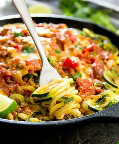 a skillet filled with pasta, meat and veggies next to lime wedges