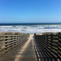 a wooden walkway leading to the beach with waves in the water and sand on either side