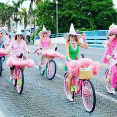 several women dressed in pink riding bikes down the street with hats on and one wearing a green dress