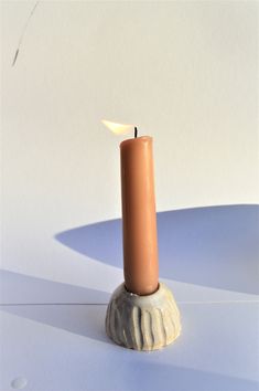 a single candle sitting on top of a white table next to a light brown pillar