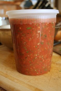 a plastic cup filled with salsa sitting on top of a wooden table