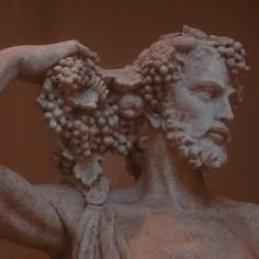 the statue has grapes on his head and is holding it in one hand with both hands