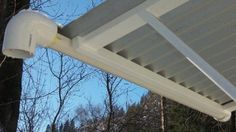 a white gutter attached to the side of a house with trees in the background