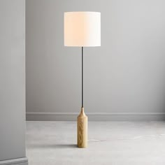 a floor lamp with a wooden base and a white shade on the top, in a room