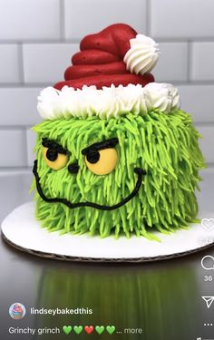 a green cake with white frosting and a red hat on it's head