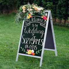 a chalkboard sign decorated with flowers and greenery for a wedding ceremony in the grass