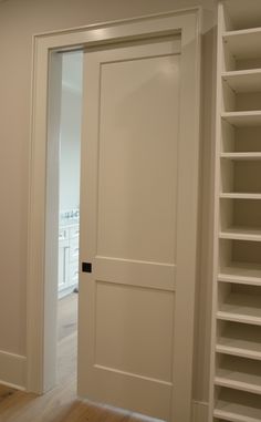 an open white door in a room with shelving on the wall and hardwood floors